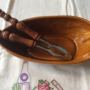 May include: A brown ceramic nut bowl with a pair of metal nutcrackers with wooden handles.