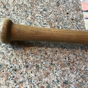 Pu&ograve; includere: Primo piano della maniglia in legno di una mazza da baseball. La maniglia &egrave; di colore marrone chiaro e ha una finitura liscia.