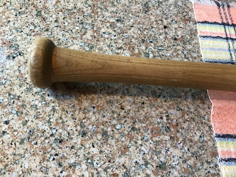 Pu&ograve; includere: Primo piano della maniglia in legno di una mazza da baseball. La maniglia &egrave; di colore marrone chiaro e ha una finitura liscia.