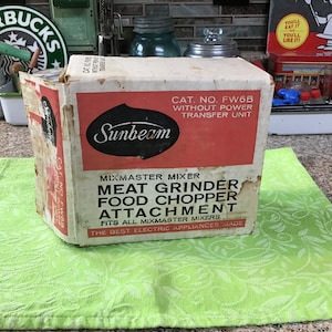 May include: A vintage Sunbeam Mixmaster meat grinder and food chopper attachment box. The box is white with red and black text. The text reads "Mixmaster Mixer Meat Grinder Food Chopper Attachment Fits all Mixmaster Mixers The Best Electric Appliances Made". The box is labeled "Cat. No. FW6B Without Power Transfer Unit".