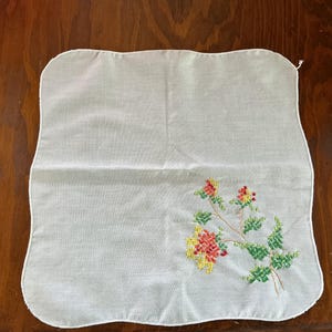 Puede incluir: Pa&ntilde;uelo cuadrado blanco con un dise&ntilde;o de bordado floral en rojo, amarillo y verde. Las flores y hojas bordadas est&aacute;n en una rama. Los bordes del pa&ntilde;uelo son festoneados.