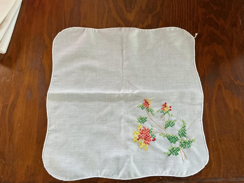 Puede incluir: Pa&ntilde;uelo cuadrado blanco con un dise&ntilde;o de bordado floral en rojo, amarillo y verde. Las flores y hojas bordadas est&aacute;n en una rama. Los bordes del pa&ntilde;uelo son festoneados.
