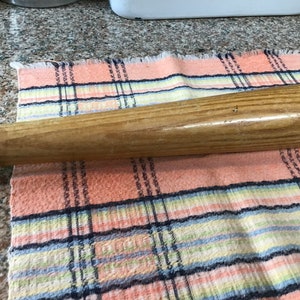 Pu&ograve; includere: Una mazza da baseball in legno con finitura naturale. La mazza &egrave; appoggiata su un panno a quadri rosa e bianco.