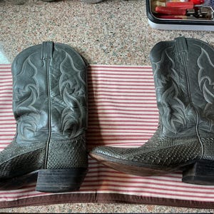 May include: A pair of grey cowboy boots featuring a textured snakeskin-patterned leather foot and a smooth leather shaft with decorative tonal stitching. The boots have a pointed toe, a stacked block heel, and a pull-on design with side tabs.