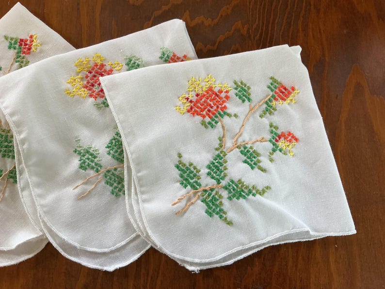 Puede incluir: Un conjunto de pa&ntilde;uelos blancos con dise&ntilde;os florales bordados. Las flores son rojas y amarillas, con hojas y tallos verdes. El bordado es detallado y a&ntilde;ade un toque vintage a los pa&ntilde;uelos.