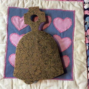 May include: A wooden bell with a carved floral design, sitting on a white and blue quilted fabric with pink hearts.
