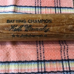 Pu&ograve; includere: Una mazza da baseball in legno con il testo "Batting Champion" e la firma "Keith Hernandez" con il testo "Little League" sotto.