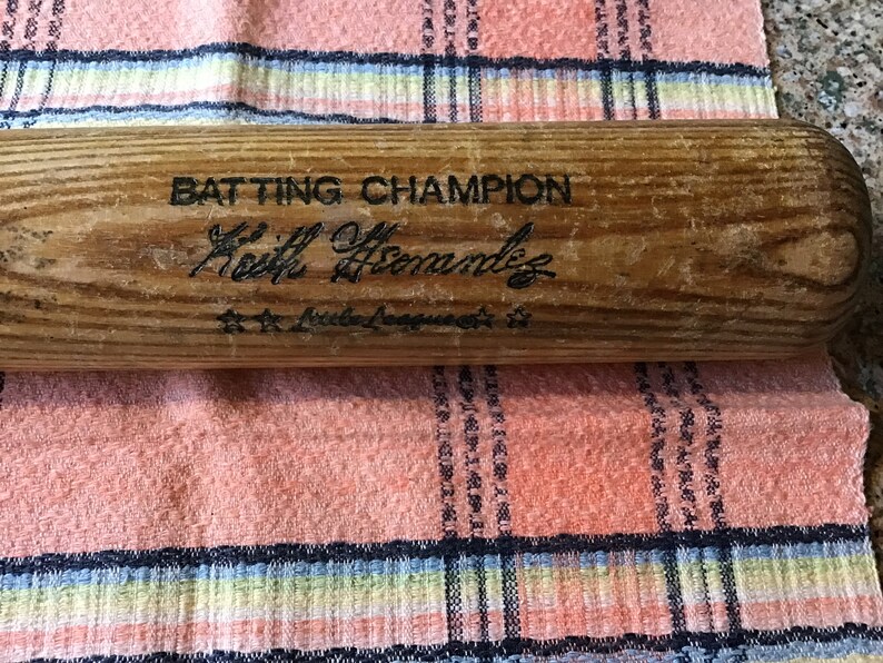 Pu&ograve; includere: Una mazza da baseball in legno con il testo "Batting Champion" e la firma "Keith Hernandez" con il testo "Little League" sotto.