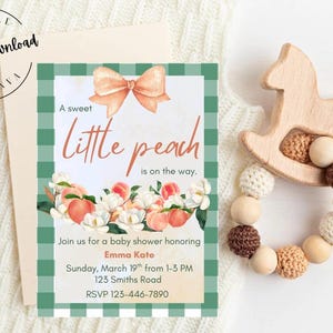 May include: A baby shower invitation with a peach theme. The invitation features a peach bow, the text "A sweet little peach is on the way," and floral and peach illustrations. A wooden rocking horse teether is next to the invitation.