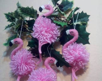 Può includere: Quattro decorazioni di fenicottero rosa in feltro con corpi a pompon e occhi neri. Le decorazioni sono appese a un ramo verde frondoso.