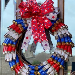 May include: A red, white, and blue patriotic wreath made of shotgun shells. The wreath is decorated with a red, white, and blue bow with white stars.