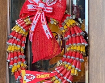 May include: A red, white, and yellow Chiefs wreath made of shotgun shells with a red bow and a Kansas City Chiefs sign.
