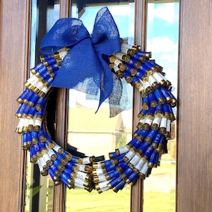 May include: A blue and white wreath made of shotgun shells with a blue burlap bow.