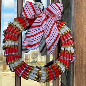 May include: A Christmas wreath made of shotgun shells with a red and white striped bow.