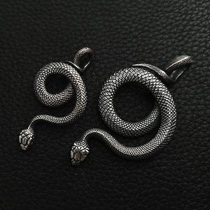 以下が含まれることがあります： 鱗と頭部が詳細に描かれた銀製の蛇のペンダント2つ。蛇は絡み合っており、1つは円形になっている。