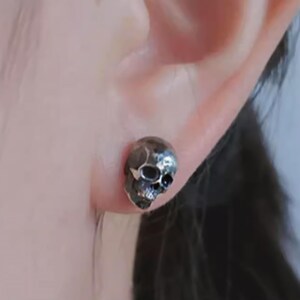 Pu&ograve; includere: Un orecchino a forma di teschio in argento con un design dettagliato. L'orecchino &egrave; indossato sul lobo dell'orecchio sinistro.