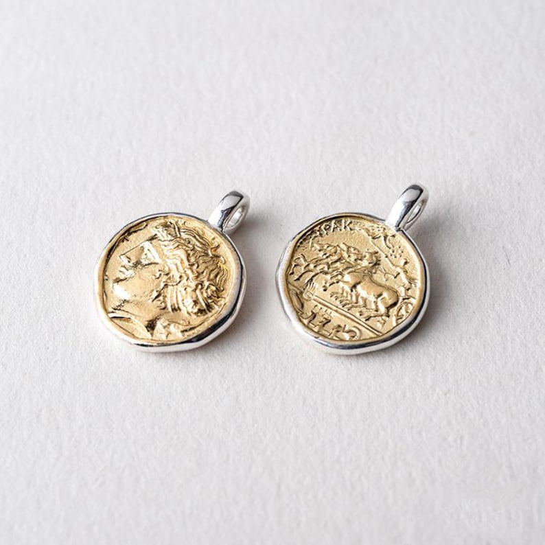 May include: Two gold-toned coin pendants with silver rims. One pendant features a profile of a person's head, the other features a horse-drawn chariot.