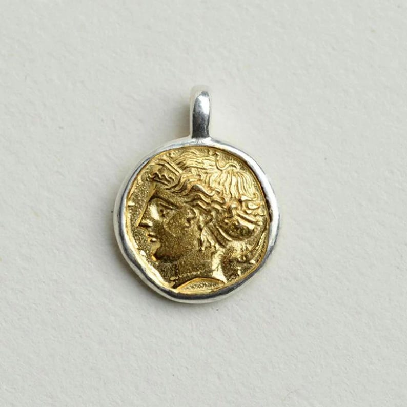 May include: A gold and silver pendant featuring a profile of a woman's face. The pendant is round and has a textured edge.