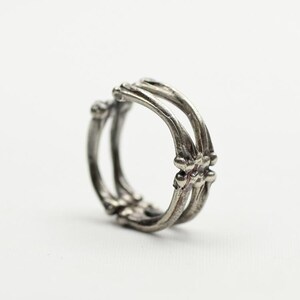 Puede incluir: Un anillo de plata con un diseño único e intrincado. El anillo está hecho de múltiples bandas entrelazadas que crean un patrón delicado e intrincado.