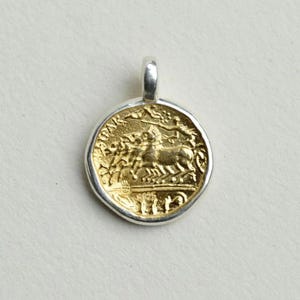 May include: A gold-plated silver pendant featuring a Roman coin design with a chariot and horses. The pendant is round and has a silver bail.