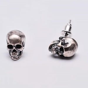 Pu&ograve; includere: Un paio di orecchini a forma di teschio in argento. Ogni orecchino presenta un design di teschio dettagliato con un perno e un retro a farfalla.