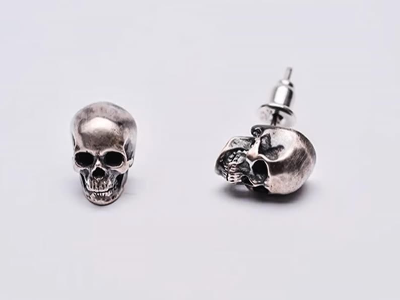 Pu&ograve; includere: Un paio di orecchini a forma di teschio in argento. Ogni orecchino presenta un design di teschio dettagliato con un perno e un retro a farfalla.