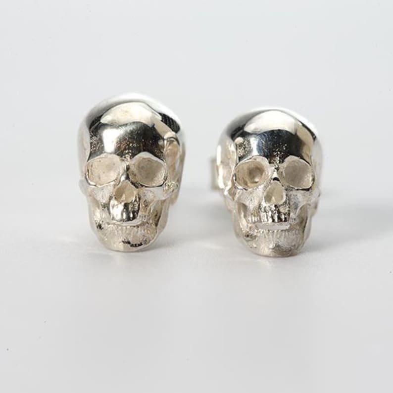 Pu&ograve; includere: Un paio di orecchini a forma di teschio in argento. I teschi sono dettagliati e hanno un aspetto realistico.