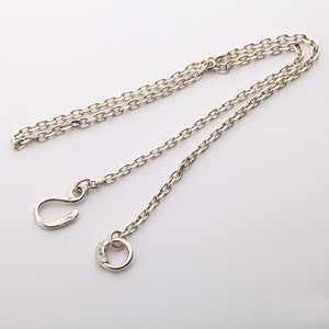 May include: A silver chain necklace with two different clasps. One clasp is a hook and the other is a round ring.
