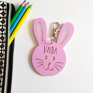 May include: Pink bunny-shaped keychain with the name "VAIDA" cut out. The keychain has a silver metal ring.