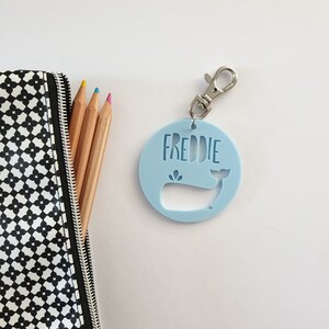 May include: A light blue whale-shaped keychain with a silver clip and the name "FREDDIE" printed on it.