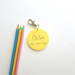 May include: Yellow round keychain with a silver clip and the name "Chloe" written in gold lettering with a small heart and arrows on either side.