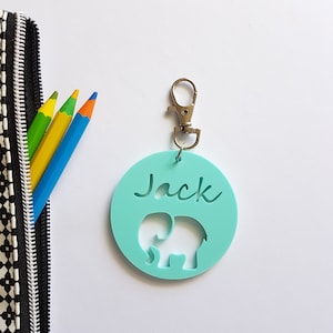 May include: A light blue round keychain with an elephant cutout and the name "Jack" written in cursive. The keychain has a silver metal clasp.