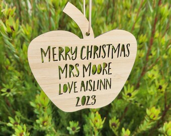 May include: A wooden apple-shaped Christmas ornament with the text "Merry Christmas Mrs Moore Love Aislinn 2023" cut out.