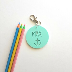 May include: A light blue round keychain with the name "MAX" and an anchor design. The keychain has a silver metal ring.