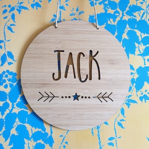 a round bamboo name plaque that comes in two sizes, 14cm or 19.5cm in diameter.  It is personalised with a name and features a star and arrow design