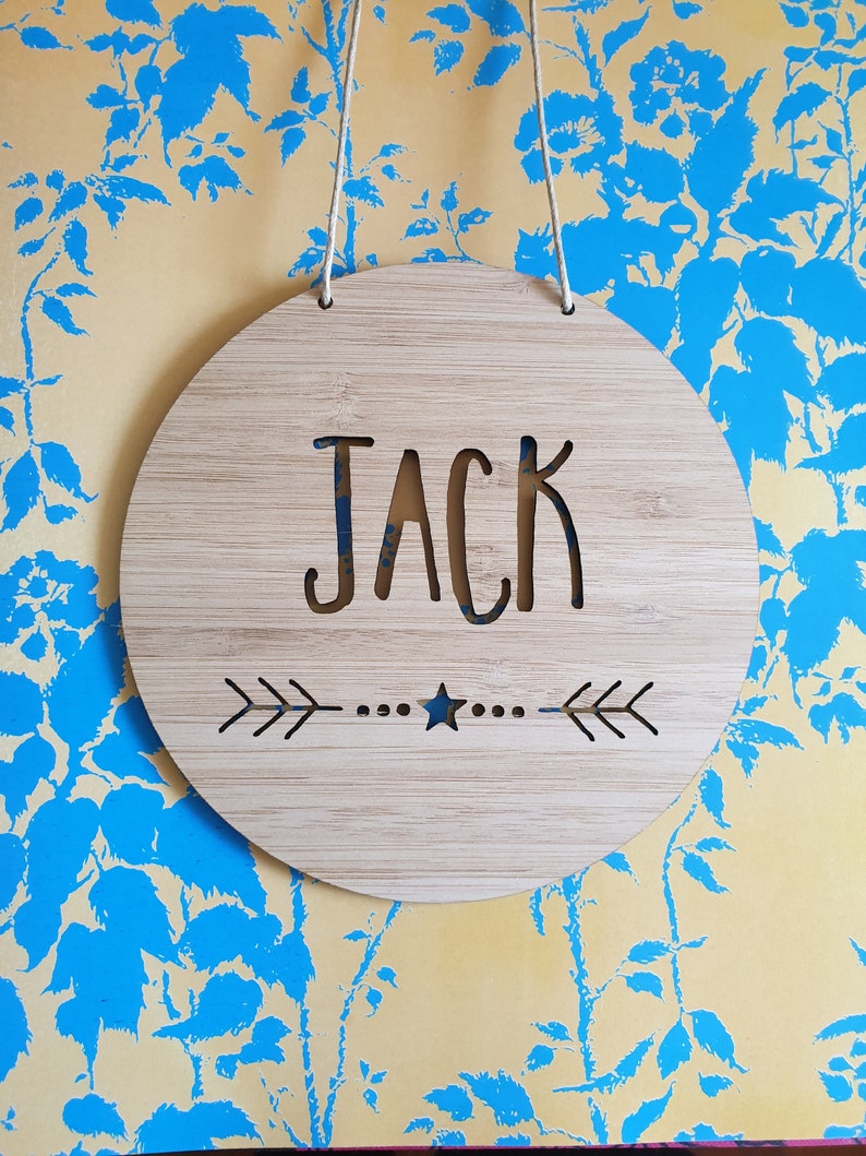 a round bamboo name plaque that comes in two sizes, 14cm or 19.5cm in diameter.  It is personalised with a name and features a star and arrow design