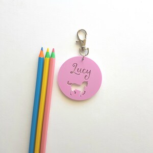 May include: Pink round keychain with a horse silhouette and the name "Lucy" written in cursive. The keychain has a silver metal ring and clip.