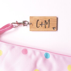 May include: A wooden keychain with a light brown finish and a silver clasp. The keychain has the letters "C+M" engraved on it, along with a small heart.
