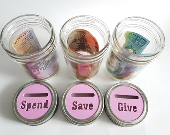 May include: Three glass jars with pink lids labeled "Spend", "Save", and "Give". Each jar contains rolled-up Australian dollar bills.
