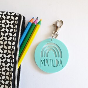 May include: A light blue round keychain with a rainbow cutout and the name "MATILDA" written in white. The keychain has a silver metal clasp.