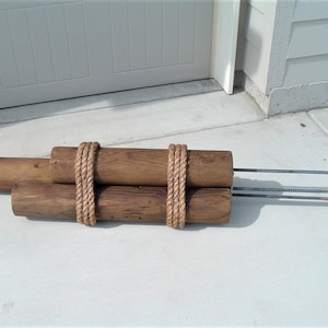 May include: Three brown wooden posts tied together with thick rope. The posts have metal rods protruding from the ends.