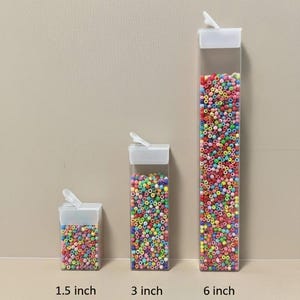 May include: Three clear rectangular plastic containers filled with multicolored beads, each featuring a white flip-top lid. The containers are labeled with heights of 1.5 inch, 3 inch, and 6 inch, indicating their respective sizes for storage.