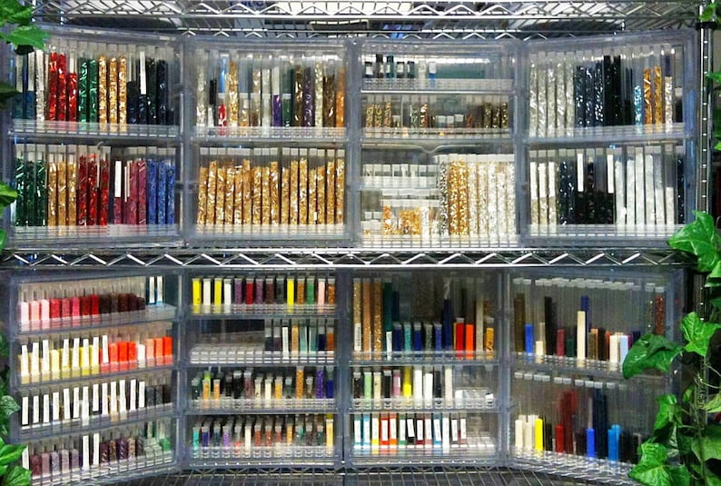 May include: A metal shelving unit filled with clear glass tubes containing various colors of small beads. The beads are organized by color and are arranged in rows on the shelves.