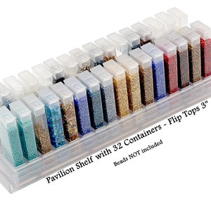 May include: A clear plastic storage shelf with 32 containers for beads. The containers are labeled "Flip Tops 3". The shelf is designed to hold small bead containers. Beads are not included.