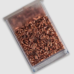 May include: A clear plastic container filled with numerous small, copper-colored metal tubes. The tubes are cylindrical with a hole through the center. The container has a clear lid and is set against a light gray background.