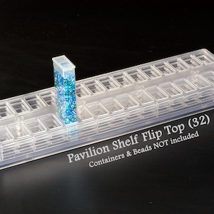 May include: A clear plastic bead storage organizer with 32 compartments. The organizer has a flip top and is labeled "Pavilion Shelf Flip Top (32)".  Containers & Beads NOT included.