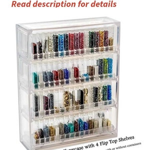 May include: Clear plastic bead storage organizer with four flip-top shelves. The organizer is filled with colorful beads. "Bead Pavilion Showcase with 4 Flip Top Shelves" and "Beads NOT included - See options; with or without containers" are printed on the bottom of the organizer.