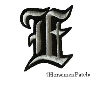 Könnte beinhalten: Schwarzer und silberner gestickter Bügelaufkleber mit dem Buchstaben "E" in alter englischer Schrift.