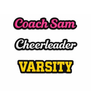 May include: Three embroidered patches with black borders. The top patch reads "Coach Sam" in pink script. The middle patch says "Cheerleader" in white script. The bottom patch says "VARSITY" in yellow block letters.