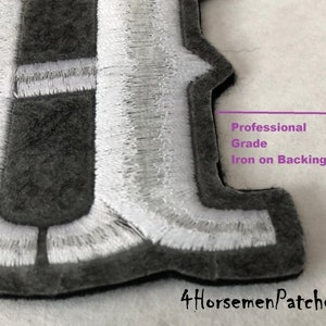 Puede incluir: Primer plano de un parche bordado en gris y blanco con la letra "F" y un respaldo termoadhesivo de calidad profesional. El parche est&aacute; hecho con materiales de alta calidad y es perfecto para agregar un toque personalizado a la ropa, bolsos u otros art&iacute;culos.